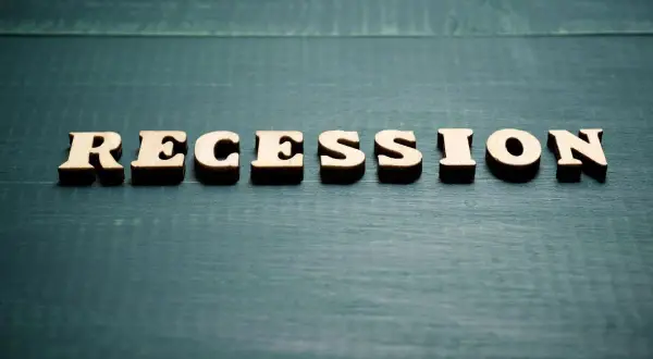 Drewniane litery układają napis "RECESSION". To słowo często pojawia się, gdy zastanawiamy się, co to znaczy recesja i jak wpływa na gospodarkę.