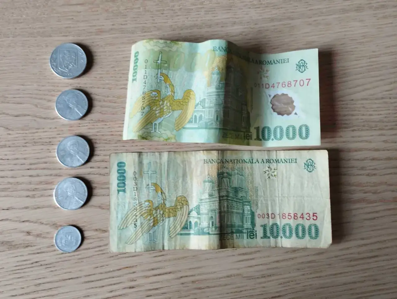 Dwie banknoty po 10 000 lej&oacute;w, rumuńska waluta, leżą obok kilku monet.